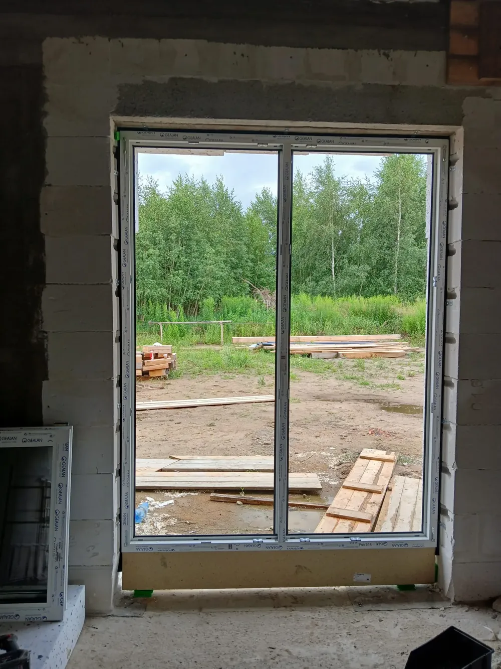 Okno PVC montowane w budynku w trakcie budowy, widok na zieleń
